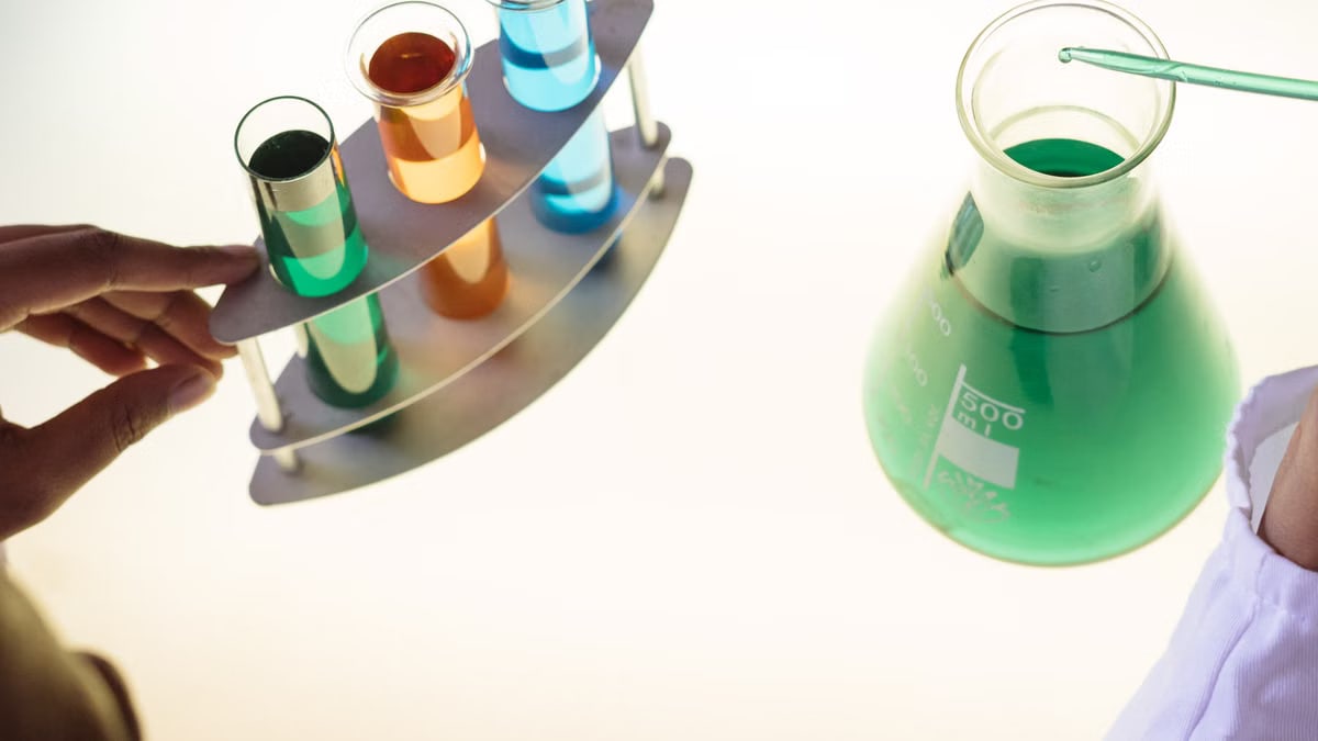 Unrecognizable ethnic scientist in white coat putting tube into flask with liquid substance while conducting chemical experiment with reagents in test tubes in laboratory